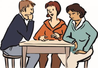 Streit-Schlichtung: Zwei Personen sitzen sich gegenüber, eine dritte Person dazwischen. Sie guckt freundlich und spricht.